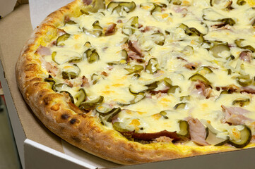 Pizza with fried appetizing crust with squid rings, bacon, pickles and lots of cheese in a box for delivery to the customer