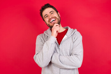 Young caucasian man wearing tracksuit over red background stares aside with wondered expression has speechless expression. Embarrassed model looks in surprise