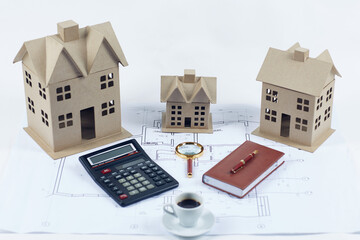 Cardboard houses calculator pen notepad magnifier coffee cup blueprints on white background