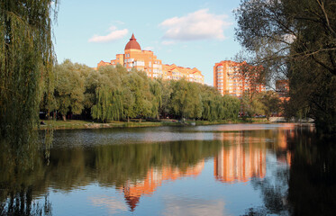 Park along small lake and modern city buildings at autumn sunset in Chabany, Kyiv, Ukraine