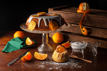 orange cake with glass foot white icing drizzled with dried orange slices sugar bowl natural oranges dark food