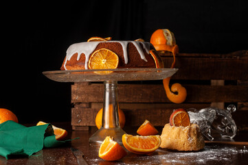 orange cake with glass foot white icing drizzled with dried orange slices sugar bowl natural oranges dark food