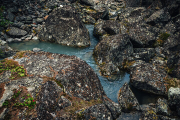 Scenic nature background of turquoise clear water stream among rocks with mosses and lichens. Atmospheric mountain landscape with mossy stones in transparent mountain creek. Beautiful mountain stream.