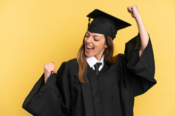 Young university graduate isolated on yellow background celebrating a victory