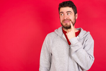 Lovely dreamy Young caucasian man wearing tracksuit over red background keeps finger near lips...
