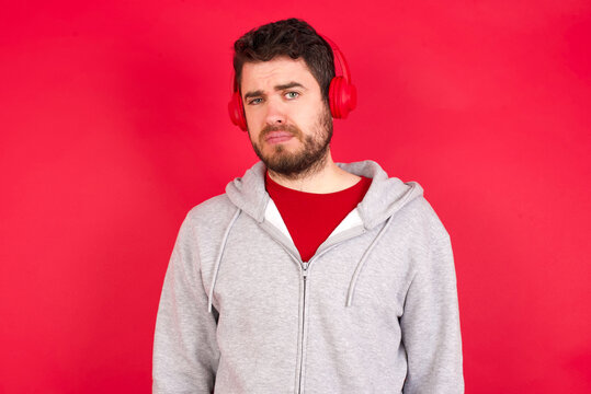 Displeased Young caucasian man wearing tracksuit over red background frowns face feels unhappy has some problems. Negative emotions and feelings concept