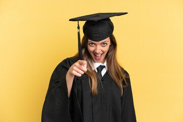 Young university graduate isolated on yellow background surprised and pointing front