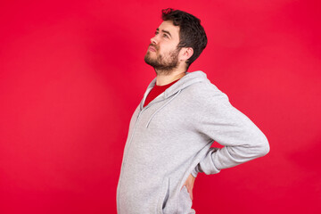 Young caucasian man wearing tracksuit over red background got back pain