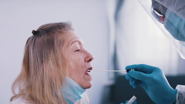 Black doctor in full uniform performing nasal swab covid tes on an elderly woman. High quality 4k footage