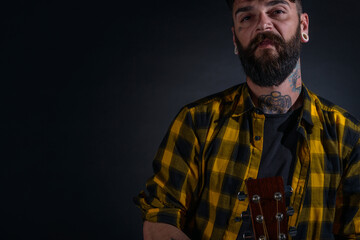 Close up portrait of a bearded man with tattoos wearing yellow black shirt and holding his guitar