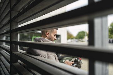Shallow focus shot of a young European man scrolling on his phone behind a fence