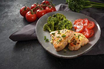 Fried tuna fillet with broccoli and tomatoes, parsley and lemon zest garnish on a gray plate and a dark slate table, copy space
