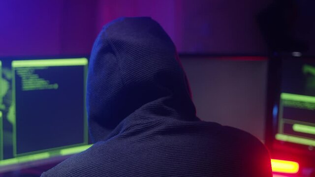 Back view of hacker sitting near computer monitors with green code screen