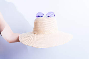woman's hand holding a summer beach hat and purple sunglasses. summer fashion concept