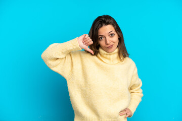Young caucasian woman isolated on blue background showing thumb down with negative expression