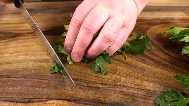 The cook cuts parsley on a wooden cutting board.