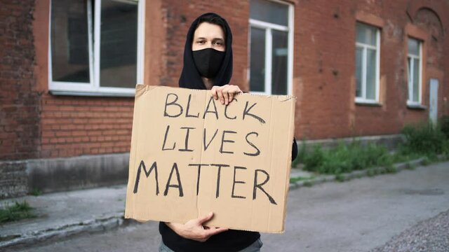 Caucasian man in mask stands with cardboard poster in hands with inscription - BLACK LIVES MATTER and NO JUSTICE NO PEACE. Single protest.