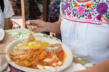 Latin Mexican woman weraing a Mexican traditional embroidered blouse, having chilaquiles with eggs and beans with spicy salsa for breakfast in the city of Ensenada Baja California.