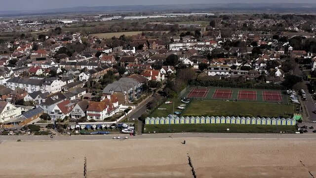Felpham seafront in West Sussex with colourful beach huts on the coast and tennis courts in the background. Aerial Footage.