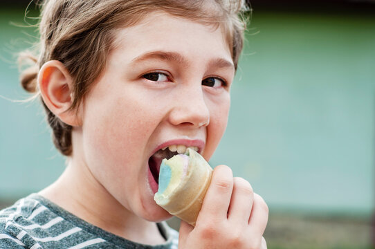 Boy with pleasure eating multicolored ice cream in a waffle cone. Cool in the summer heat. Sweet snack. Hot Summer. Emotional child licks icecream. Child with a brutal appetite bites ice cream