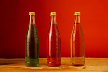 Three glass bottles - red, yellow and green-stand on a red background. Cold refreshing drink lemonade