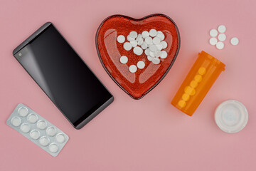 Healthcare concept with pills, smartphone, pharmacy prescription orange bottle, pink background.