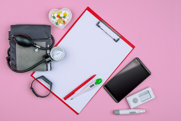 Healthcare concept with stethoscope, pills, heart, blood pressure smart watch heart rate monitor, smartphone. Empty copy space, clip board mock up, pink background.