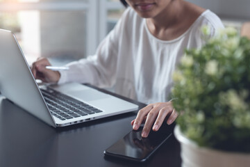 Woman working on laptop computer and using mobile phone from home office