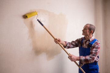 An elderly male construction worker with a mustache in a blue uniform smears the wall with a paint...