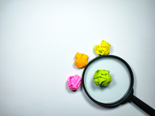 Selective focus of magnifying glass and colored crumpled paper on white background with text space.