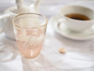 Pretty pink glass with tea and teapot on a white background