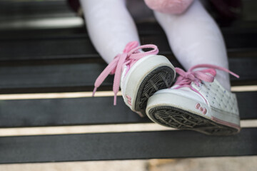Closeup of a little girl wearing small shoes with pink shoelaces sitting on a metallic bench