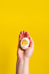 Close up on hand holding boiled egg with yolk in front of yellow background