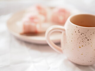 Pink mug and little pink cakes on a white bright white background.