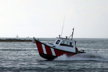 Obraz premium Red and white boat moving toward shore during overcast weather