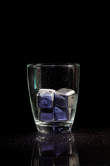 stainless steel cubes simulating ice in whisky glass on a black table.