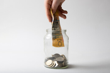 Hand holding Australian 50 dollar note over coin jar.