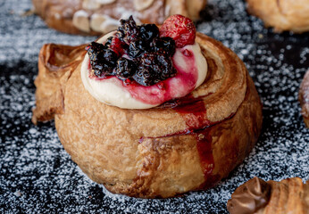 Delicious role of cheesecake croissant dough with blackberries and strawberries on top on a black table with sprinkled sugar.