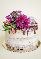 Delicious chocolate and vanilla cake decorated with white icing and purple flowers on a white table.