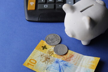 swiss banknote, coins, white piggy bank and calculator on the blue background