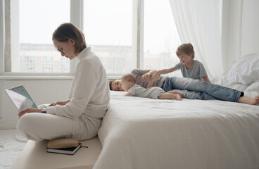 Obraz premium Busy caucasian woman trying to work while baby sitting three kids. Caucasian single mom work from home with the children. High quality photo