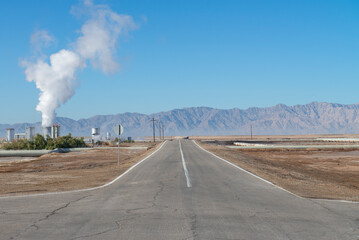 Geothermal power field with mountains in the background and the moon in the blue sky