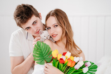 a man gave his beloved woman a bouquet of colorful tulips and a white kitten.
