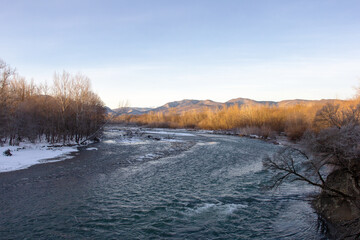 Winter in the foothills, an ice-free river on a frosty morning in the rays of the rising sun.