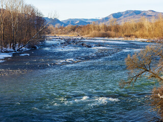Fototapeta na wymiar Winter in the foothills, an ice-free river on a frosty morning in the rays of the rising sun.