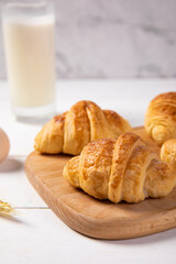 Closeup of two delicious croissants on a wooden board with a glass of milk in the background