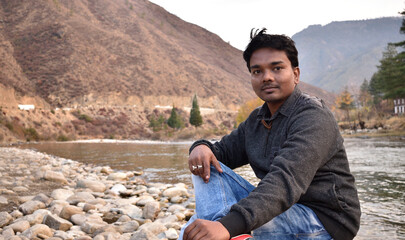 A happy man relaxing by mountain river enjoying natural landscape. Traveler backpacker sitting on...