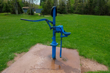 Blue hand pump for water from a well in the green field
