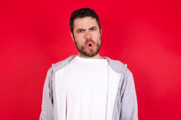 young handsome caucasian man in sports clothes against red wall expressing disgust, unwillingness, disregard having tensive look frowning face, looking indignant with something.