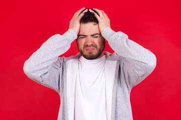 young handsome caucasian man in sports clothes against red wall holding head with hands, suffering from severe headache, pressing fingers to temples